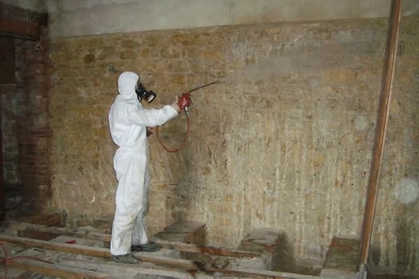 Professionnel en combinaison appliquant un traitement sur une maçonnerie